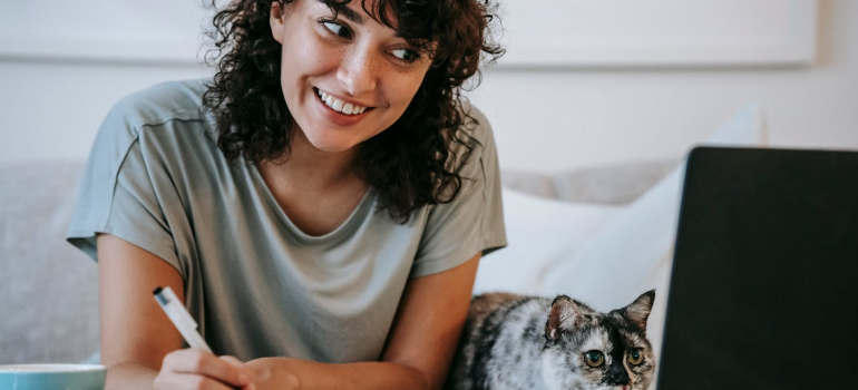 a woman looking confused while looking at a laptop screen with her cat by her side