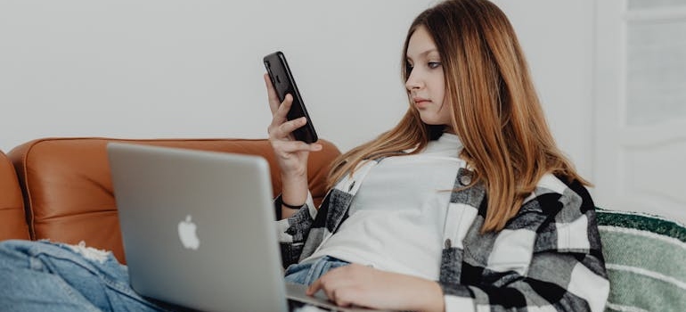 A person looking at their smarphone while using a laptop