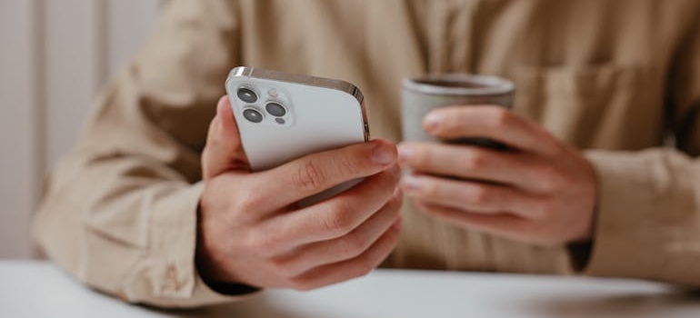 A person holding a cup and using a smartphone